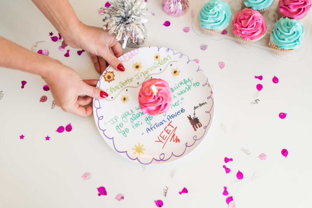 Kids birthday dinner traditions uses a white plate with colorful lyrics to a Proverb quote about going together with a pink cupcake on it, held by Dear Elly author Kelly Page, surrounded by confetti.