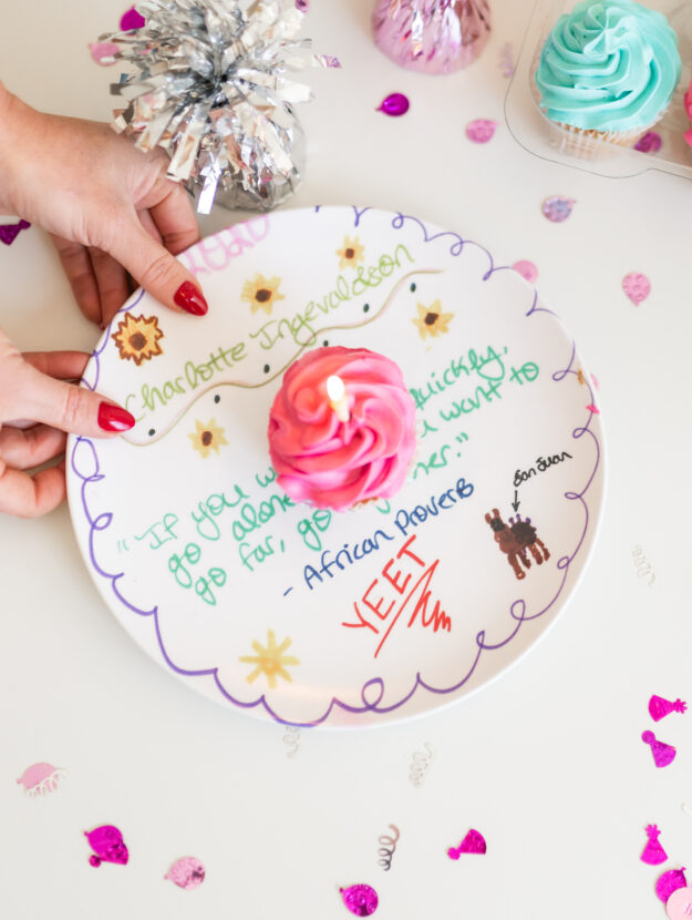 Kids birthday dinner traditions uses a white plate with colorful lyrics to a Proverb quote about going together with a pink cupcake on it, held by Dear Elly author Kelly Page, surrounded by confetti.